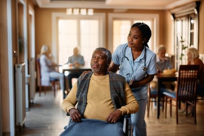 A senior resident with a caregiver in a common area