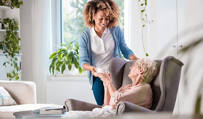 A caregiver serving tea to an elderly resident in a cozy living space