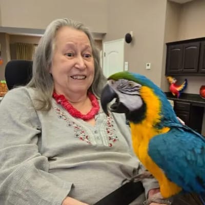 Resident smiling with a colorful parrot on her shoulder