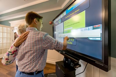 A resident and a child interacting with a digital screen in a common area