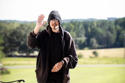 A man waving outside in a green area