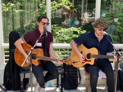 Musicians performing in a bright common area with greenery