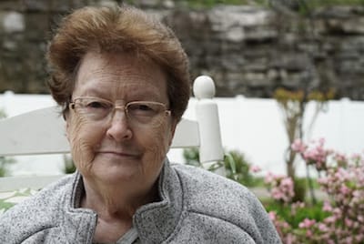 A senior woman sitting outside with flowers in the background