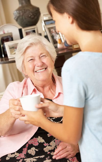 A caregiver handing a cup to a smiling resident
