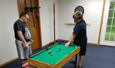 Two individuals playing billiards in an activity room