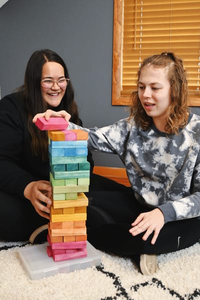 Two women playing a colorful stacking game indoors