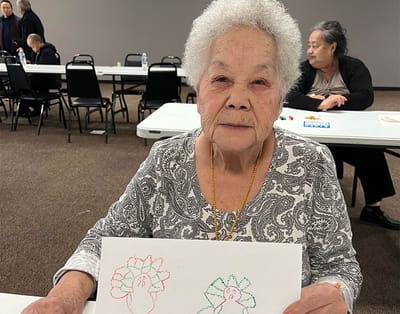 Elderly resident displaying colorful drawings at a table