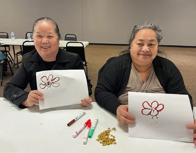 Two women holding their artworks during an activity