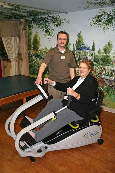 A staff member assisting a resident on a therapy bike