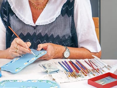 An elderly woman painting with brushes on a table