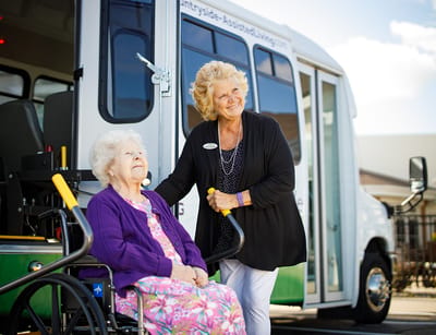 Staff assisting a resident in front of a facility transport van