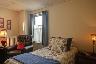 A cozy private resident room with a bed and chair