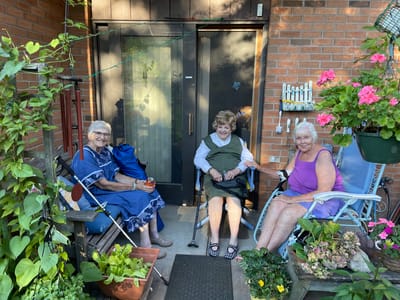 Three residents enjoying time outdoors by the entrance.