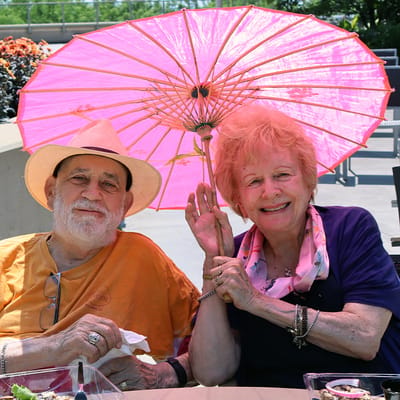 Seniors enjoying a sunny day with a pink umbrella.