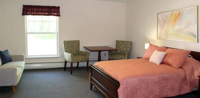 Brightly decorated resident room with bed and chairs