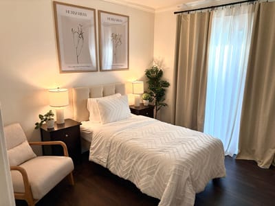 Brightly lit private room with bed and chair