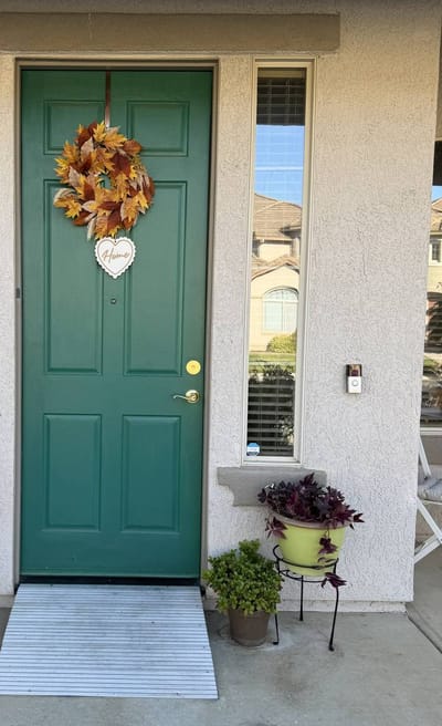 Green front door decorated with autumn wreath and plants