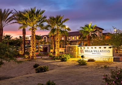 Entrance sign for Bella Villaggio with palm trees and sunset