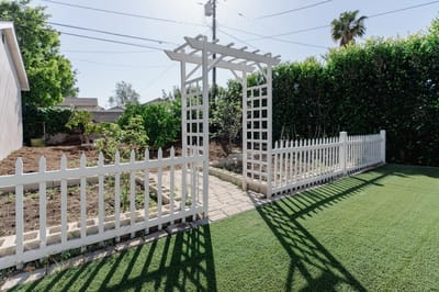 A garden entrance with a white trellis and fence