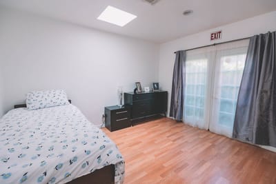 Bright, simple private resident room with a bed and exit sign