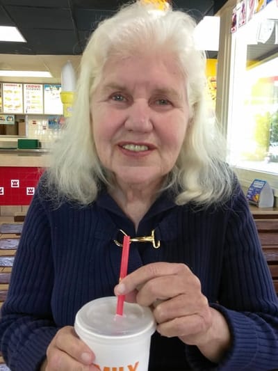 A smiling elderly woman holding a cup with a straw