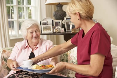 Caregiver serving food to a resident in a cozy living space