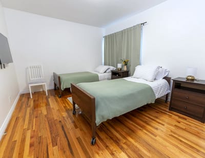 Private resident room with two beds and wood flooring