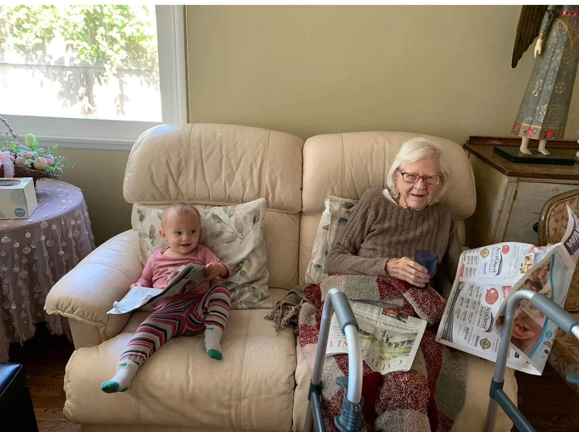 Elderly woman and baby sitting together on a couch.