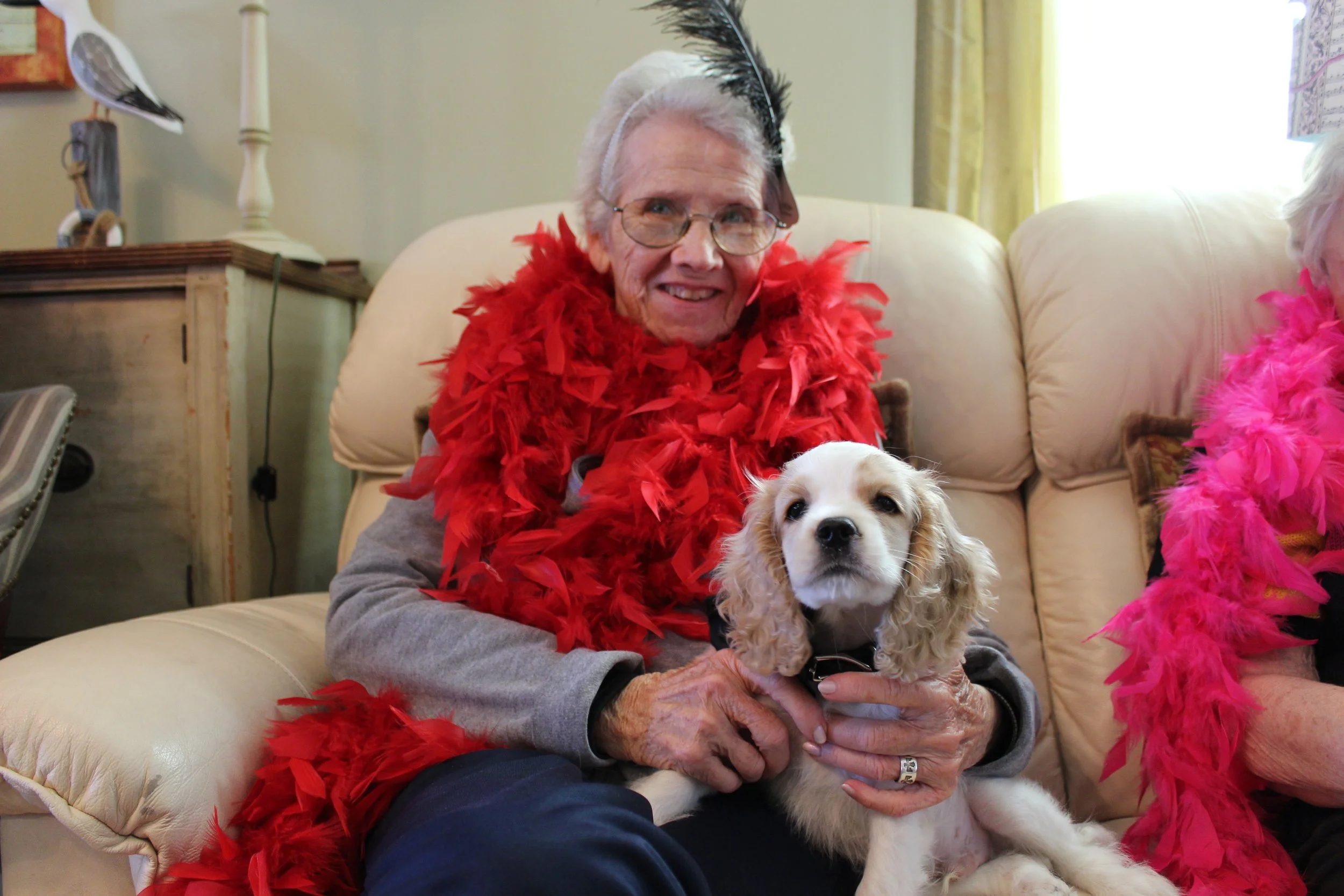 Elderly woman in a red feather boa holding a dog.