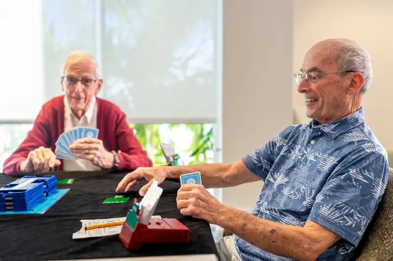 Two residents playing cards in a bright activity room