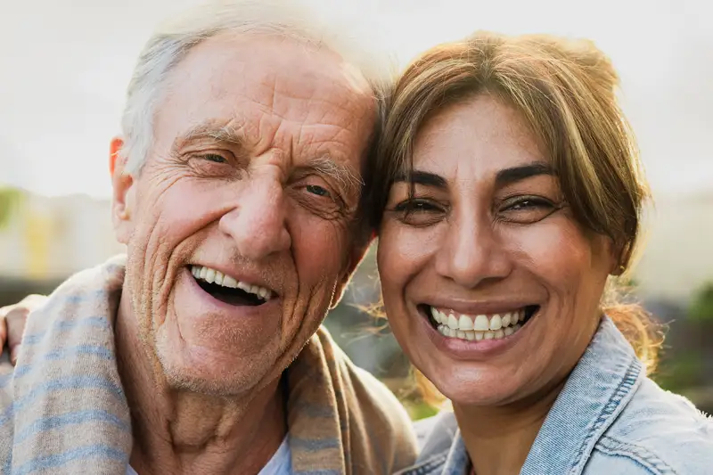 An elderly man with a caregiver smiling outdoors