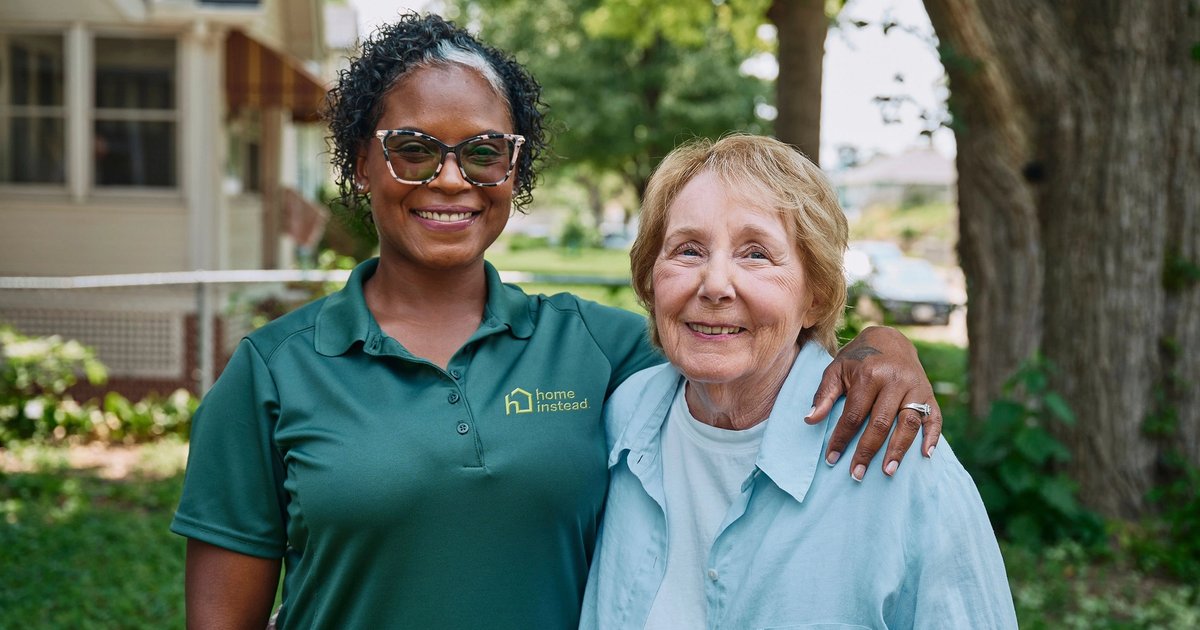 Staff member with resident outdoors, both smiling.