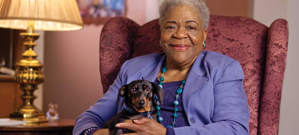 Senior woman sitting with a dog in a cozy interior setting.