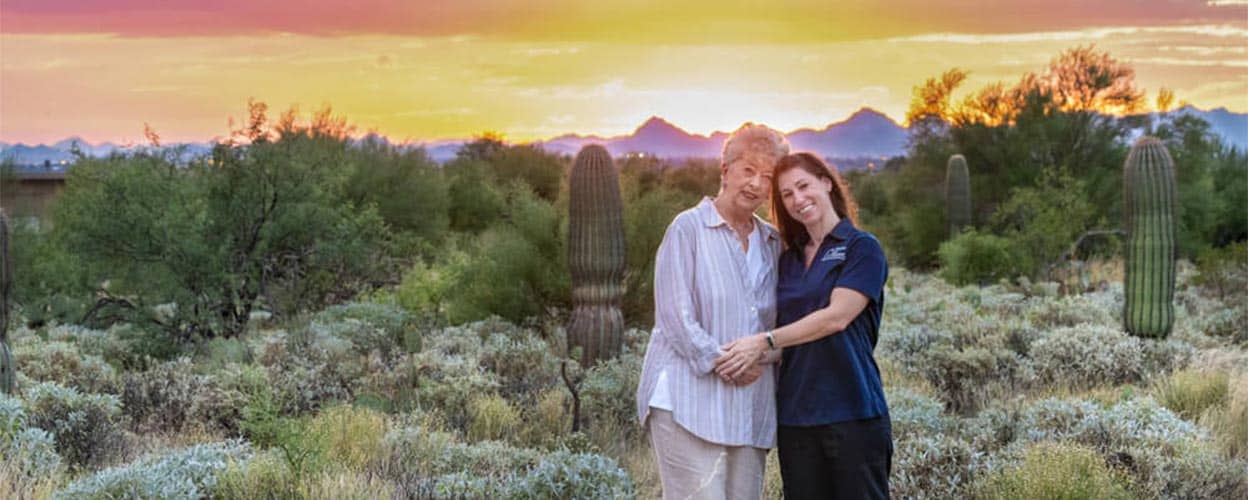 Two women smiling together outdoors at sunset.