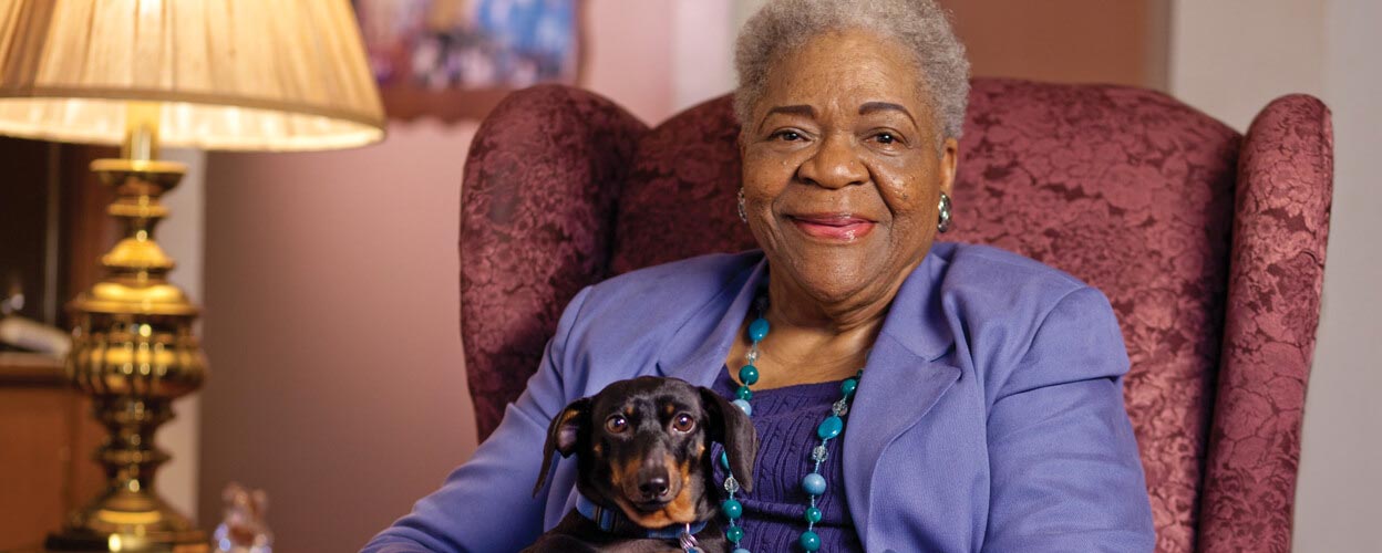 Senior woman holding a small dog in a cozy chair.