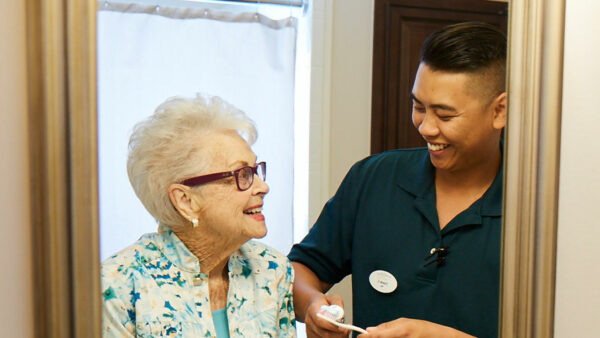 A caregiver assisting a senior woman in a bathroom mirror