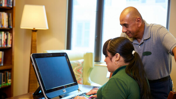 Staff assisting resident at a computer in a common area