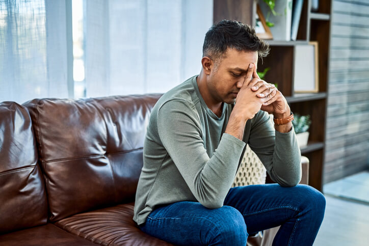 Man sitting thoughtfully on a couch in an indoor space