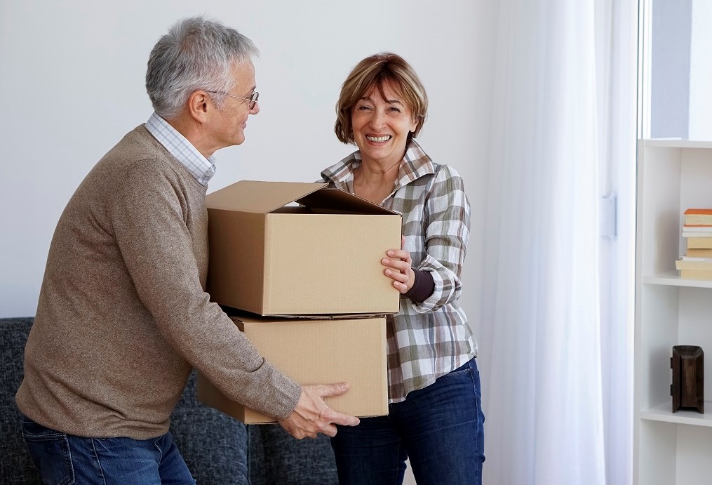 Two smiling seniors holding moving boxes together