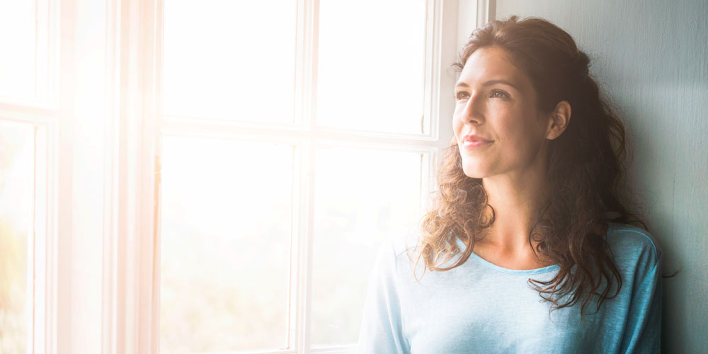 Woman looking out of a window with a contemplative expression