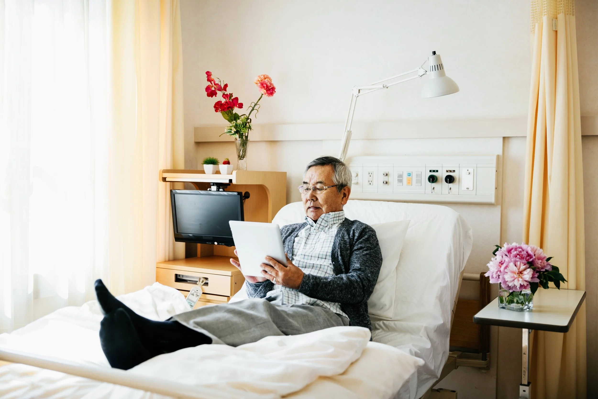 An elderly man reading on a tablet in a hospital room
