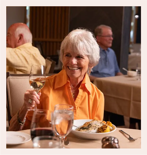 A happy resident toasting with a glass of wine in the dining room