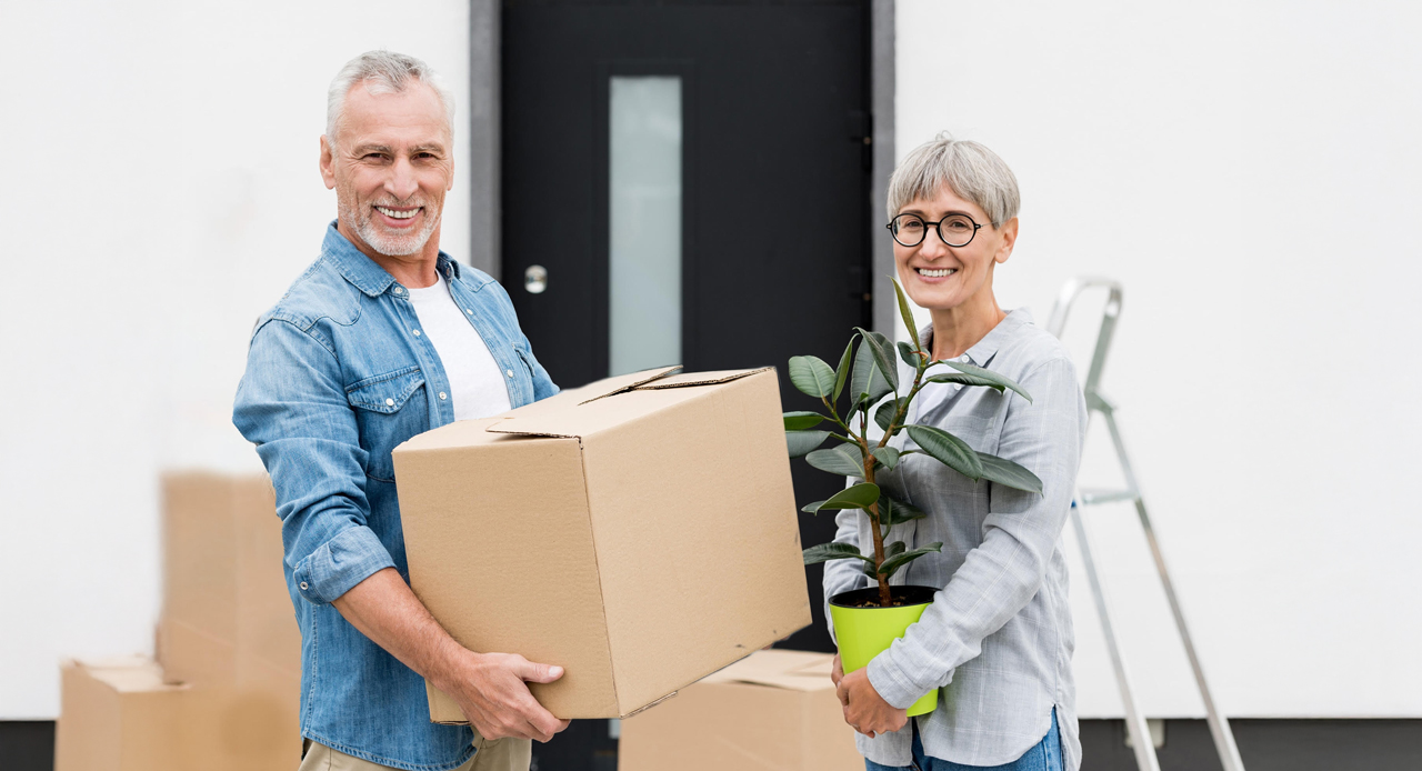 Two smiling seniors holding a box and a plant.