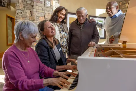 Residents enjoying music with staff at a piano