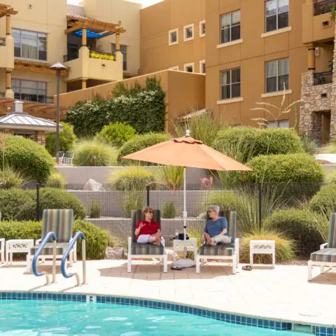 Residents relaxing by the pool with landscaped gardens