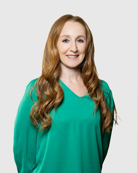 A person smiling in a green top against a gray background
