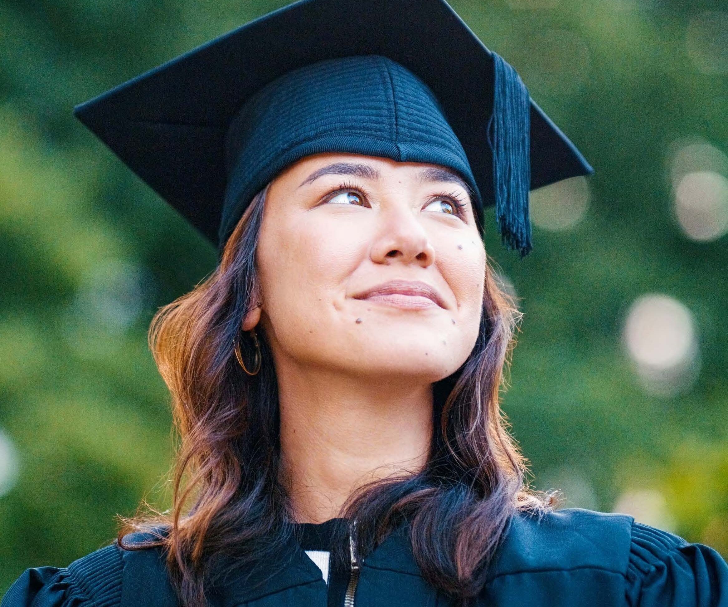 A graduate in cap and gown with a thoughtful expression