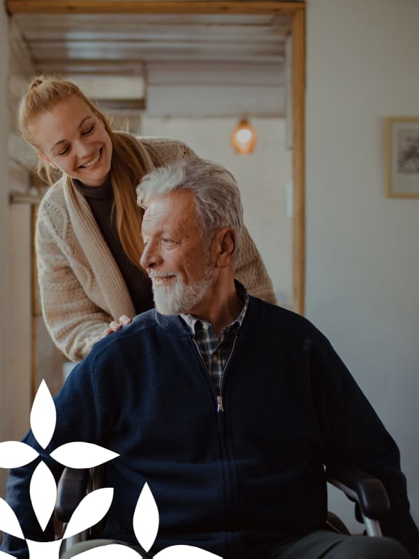 Caregiver assisting an elderly man in a cozy interior.
