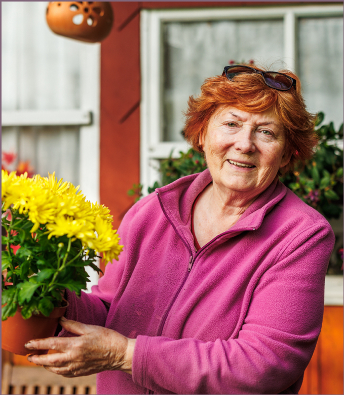 Elderly woman smiling with potted flowers.