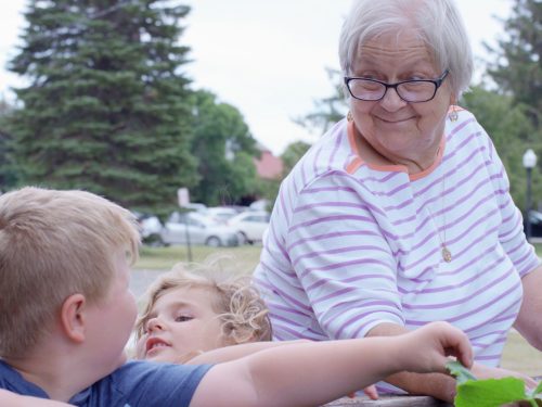 Elderly woman interacting with children outdoors.